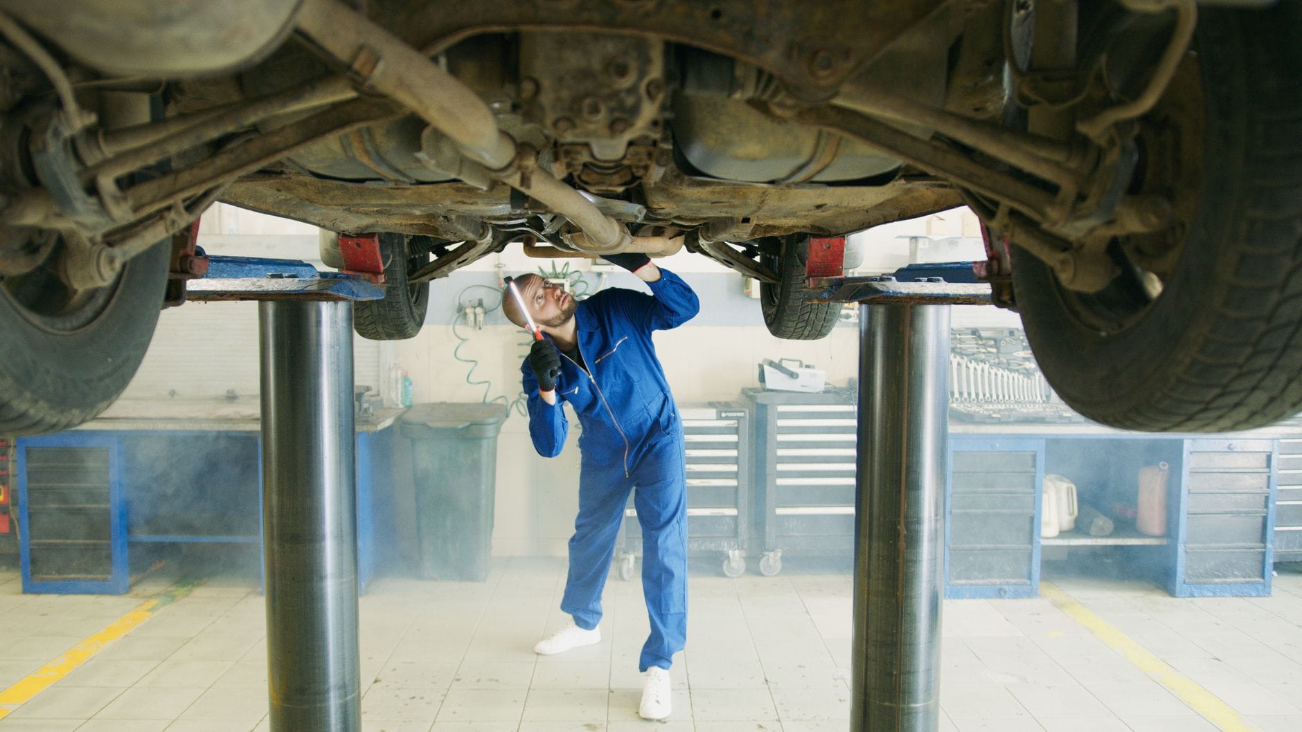 Mechanik w niebieskim kombinezonie ogląda podwozie podniesionego auta