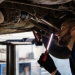 Mechanik sprawdza podwozie samochodu światłem w warsztacie